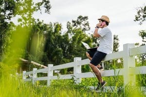 Man making a phone call while sitting on a fence and working in nature.
