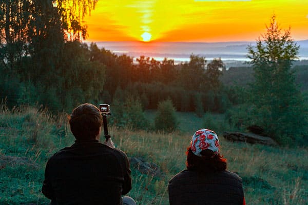 A man and a woman hiker with an action camera sitting and taking a beautiful shot of a sunrise